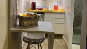 A compact kitchen with a window, a basket on the counter, and a small table with a chair. - Urban Box House (São Paulo)