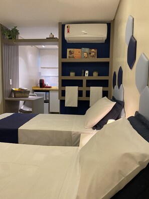 A hotel room with a bed, a desk, a chair, a shelf with decorative items, and an air conditioning unit. - Urban Box House (São Paulo)