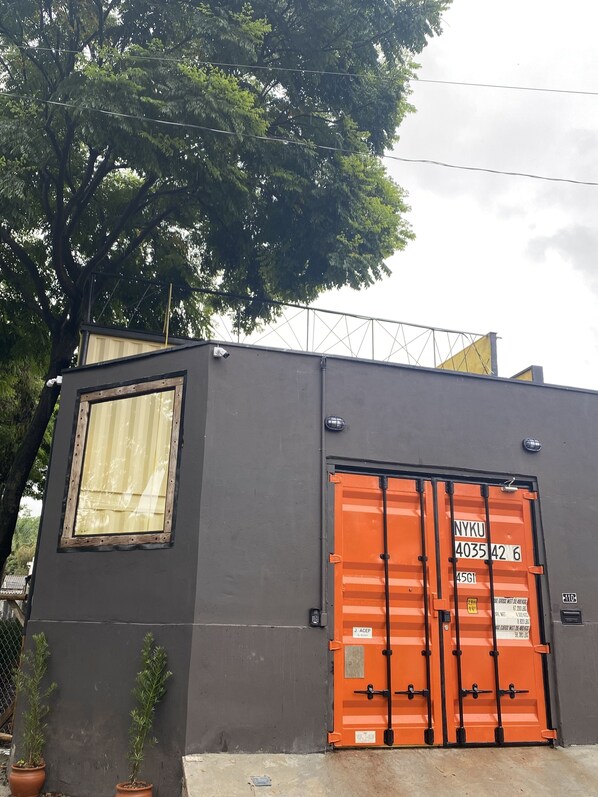 A building with a large orange shipping container door, a small window, and two potted plants.