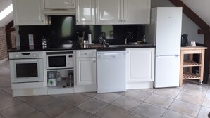 Una cocina compacta con armarios blancos, encimera negra y estante de madera.