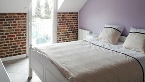Un dormitorio con techo inclinado, pared de ladrillo, cama blanca y vistas a través de una puerta.