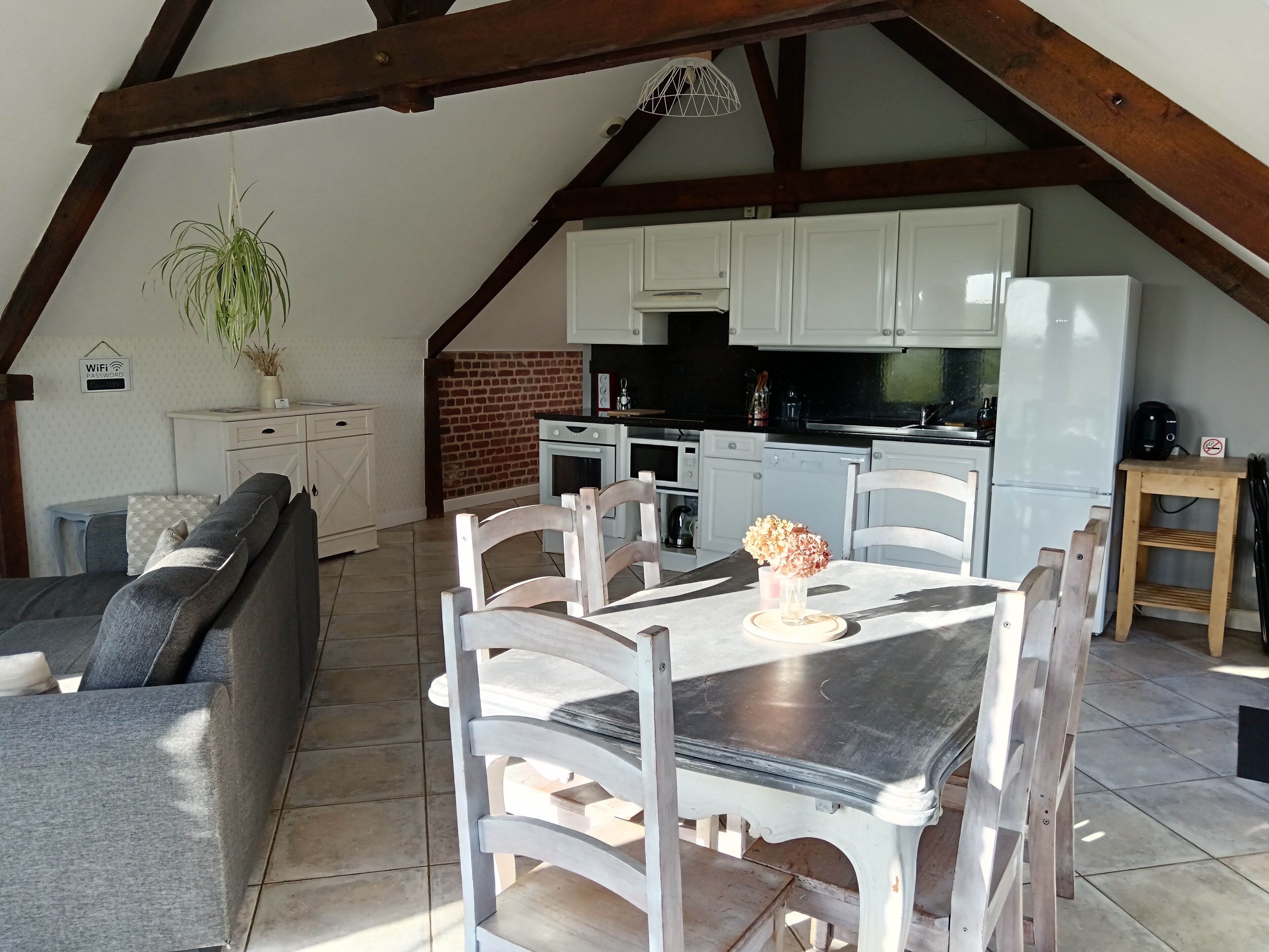 Een gezellige keuken in loft-stijl met witte kasten, een eettafel met stoelen en een hangplant.