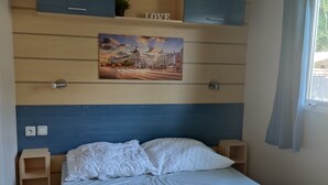 Ein Schlafzimmer mit einem Bett, einem Kopfteil, einem Regal mit einem Gemälde und einem Fenster mit Vorhängen.
