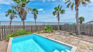 A rectangular swimming pool with stone edging, surrounded by a wooden fence and palm trees. - Ohana GetAway is the perfect tropical retreat for your party of 10—and it’s pet (Port Aransas)