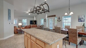 A spacious kitchen with a granite countertop, wooden cabinets, and a dining area with wicker chairs. - Ohana GetAway is the perfect tropical retreat for your party of 10—and it’s pet (Port Aransas)