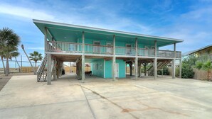A two-story building with a balcony, a covered outdoor area, and a concrete driveway. - Ohana GetAway is the perfect tropical retreat for your party of 10—and it’s pet (Port Aransas)