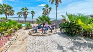A patio with stone flooring, a circular table with chairs, and palm trees. - Ohana GetAway is the perfect tropical retreat for your party of 10—and it’s pet (Port Aransas)
