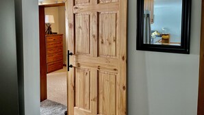 A wooden sliding door with a black handle, a framed mirror on the wall, and a wooden dresser with a lamp in the background. - Relaxing Ranch Style Waterfront Home--30 minutes from Ann Arbor (Pinckney)