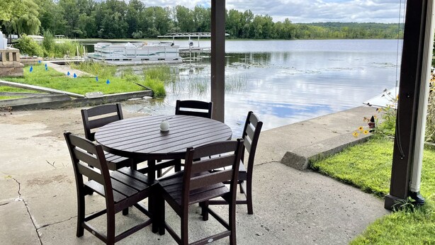 A covered outdoor seating area with a table and chairs, overlooking a lake with boats and docks. - Relaxing Ranch Style Waterfront Home--30 minutes from Ann Arbor (Pinckney)