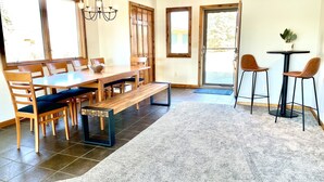 A dining area with a wooden table and chairs, a bench, and a small table with two stools. - Relaxing Ranch Style Waterfront Home--30 minutes from Ann Arbor (Pinckney)