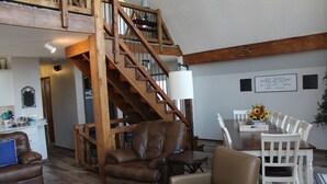 A spacious living area with a wooden staircase, leather armchairs, a dining table with white chairs, and a chandelier. - Beautiful, Majestic Log Cabin Large Game Room and Lake View (Wagoner)