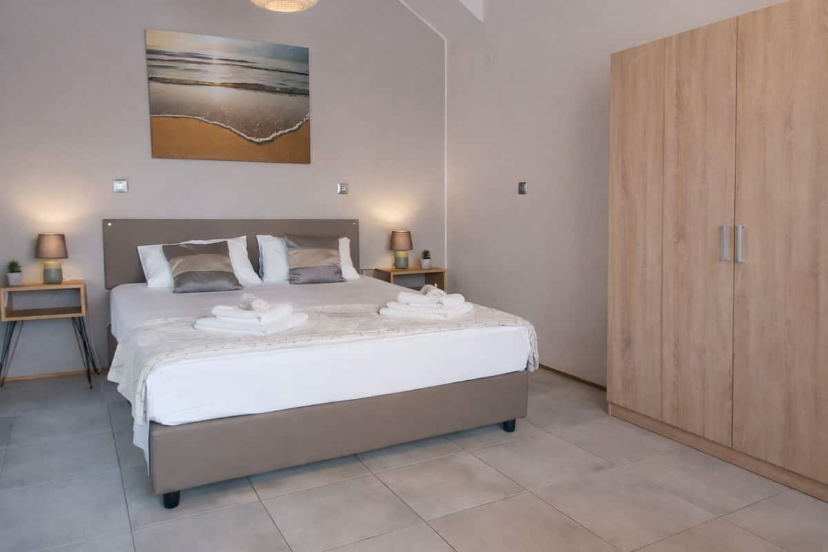 A bedroom with a bed, bedside tables, a nightstand, a wardrobe, and a painting on the wall.