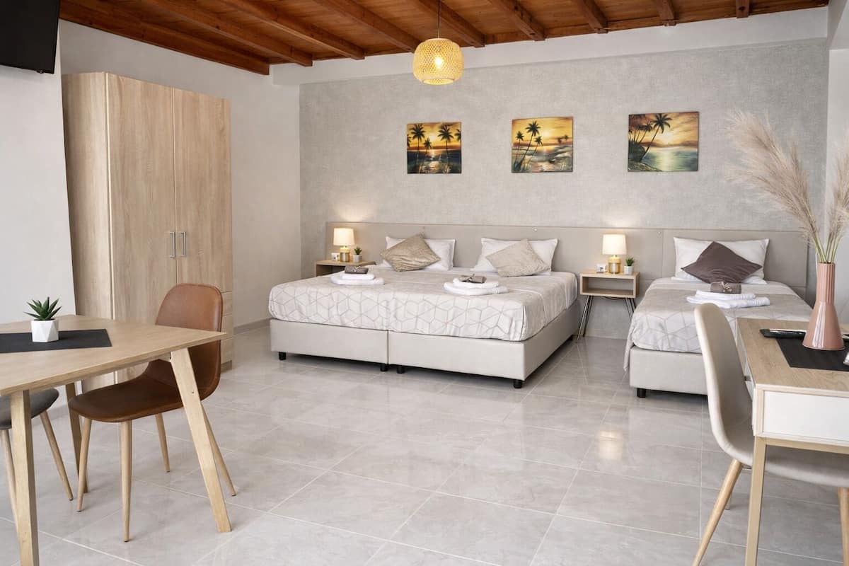 A bedroom with two beds, a wooden wardrobe, a dining table with chairs, and artwork on the wall.