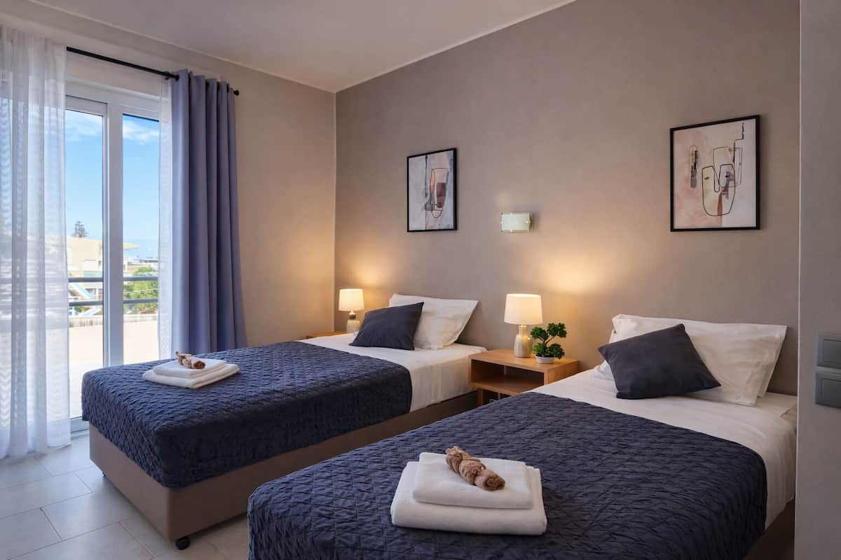 A hotel room with two beds, a balcony, and artwork on the walls.