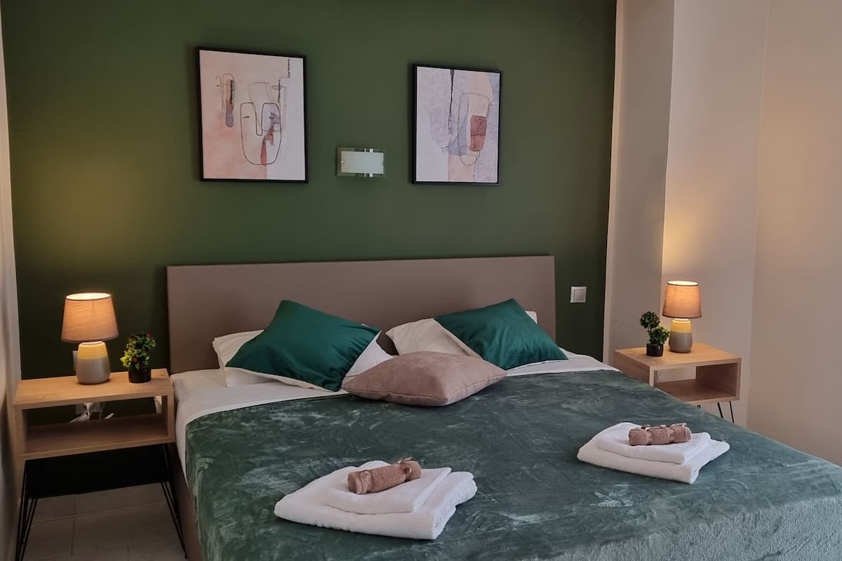 A hotel room with a bed, two nightstands, two wall-mounted lamps, a green headboard, and two framed artworks.