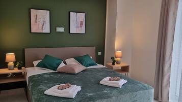 Habitación de hotel con cama, dos mesitas de noche, dos lámparas de pared, cabecera verde y dos obras de arte enmarcadas.