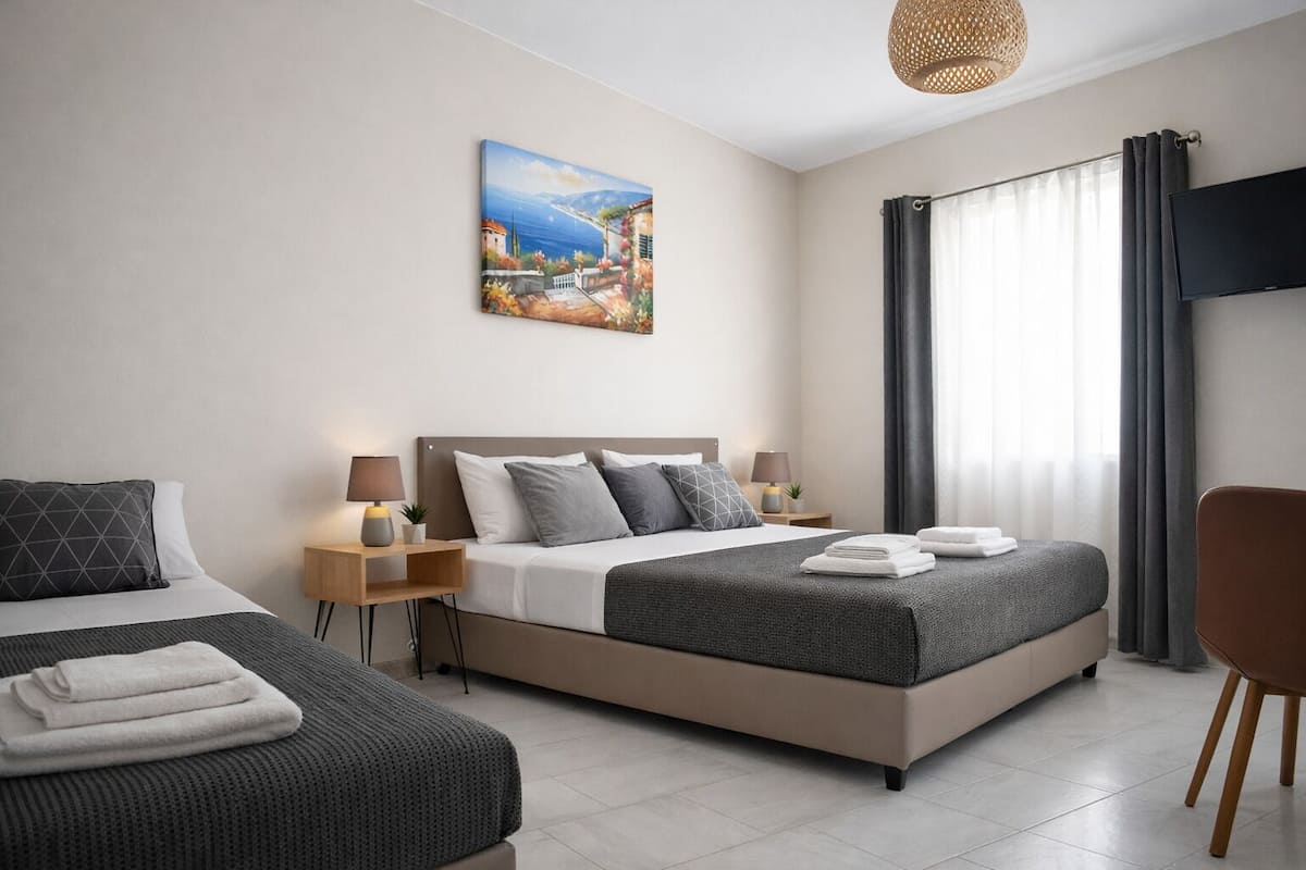 A hotel room with two beds, a painting, a TV, and a window with curtains.