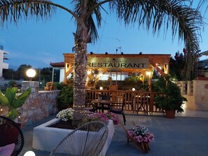 A restaurant with outdoor seating, a stone pillar, and string lights. - Secret Garden Hotel (Platanias)