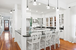A spacious kitchen with white cabinetry, a central island with bar stools, and pendant lighting. - Complimentary LSV in WaterColor- 250 Needlerush by Royal Destinations (Watercolor)