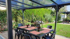A covered patio with a table and chairs, surrounded by greenery and a barbecue grill. - GITE DU SUD DE L'AISNE Rated 3 stars by Aisne tourisme. (Hautevesnes)