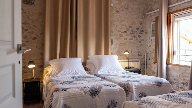 A bedroom with two beds, a stone wall, a window with curtains, and a nightstand with a lamp. - GITE DU SUD DE L'AISNE Rated 3 stars by Aisne tourisme. (Hautevesnes)