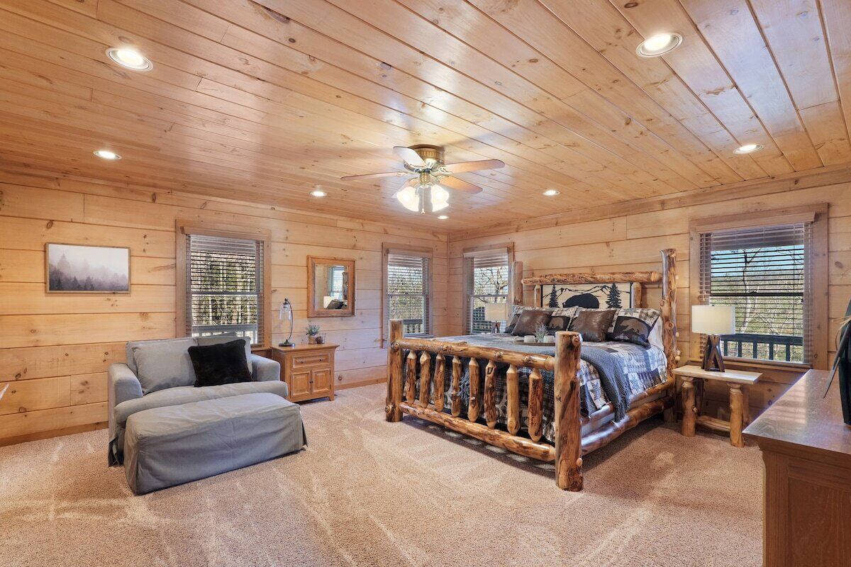 Ein Schlafzimmer in einer Blockhütte mit einem hölzernen Bett, einer Couch, einem Schreibtisch und einem Deckenventilator.