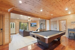 A wooden interior with a pool table, a stone fireplace, and a television mounted on the wall.