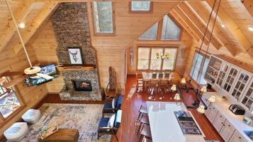 A spacious log cabin interior with a stone fireplace, wooden dining area, and large windows.