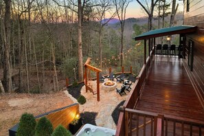A wooden deck with outdoor seating and a fire pit, surrounded by a forested area.