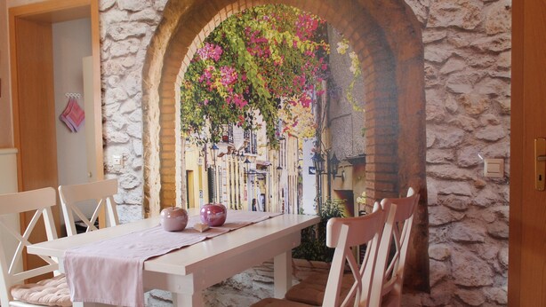 A dining area with a stone wall, an archway with flowers, and a table with chairs. - Comfortable apartment on the Zollernalb for families, single travelers, workers, .... (Meßstetten)