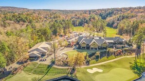 Un campo de golf con un club de campo, un estanque y zonas boscosas circundantes.