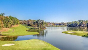 Un campo de golf con obstáculos acuáticos y un club de campo al fondo.