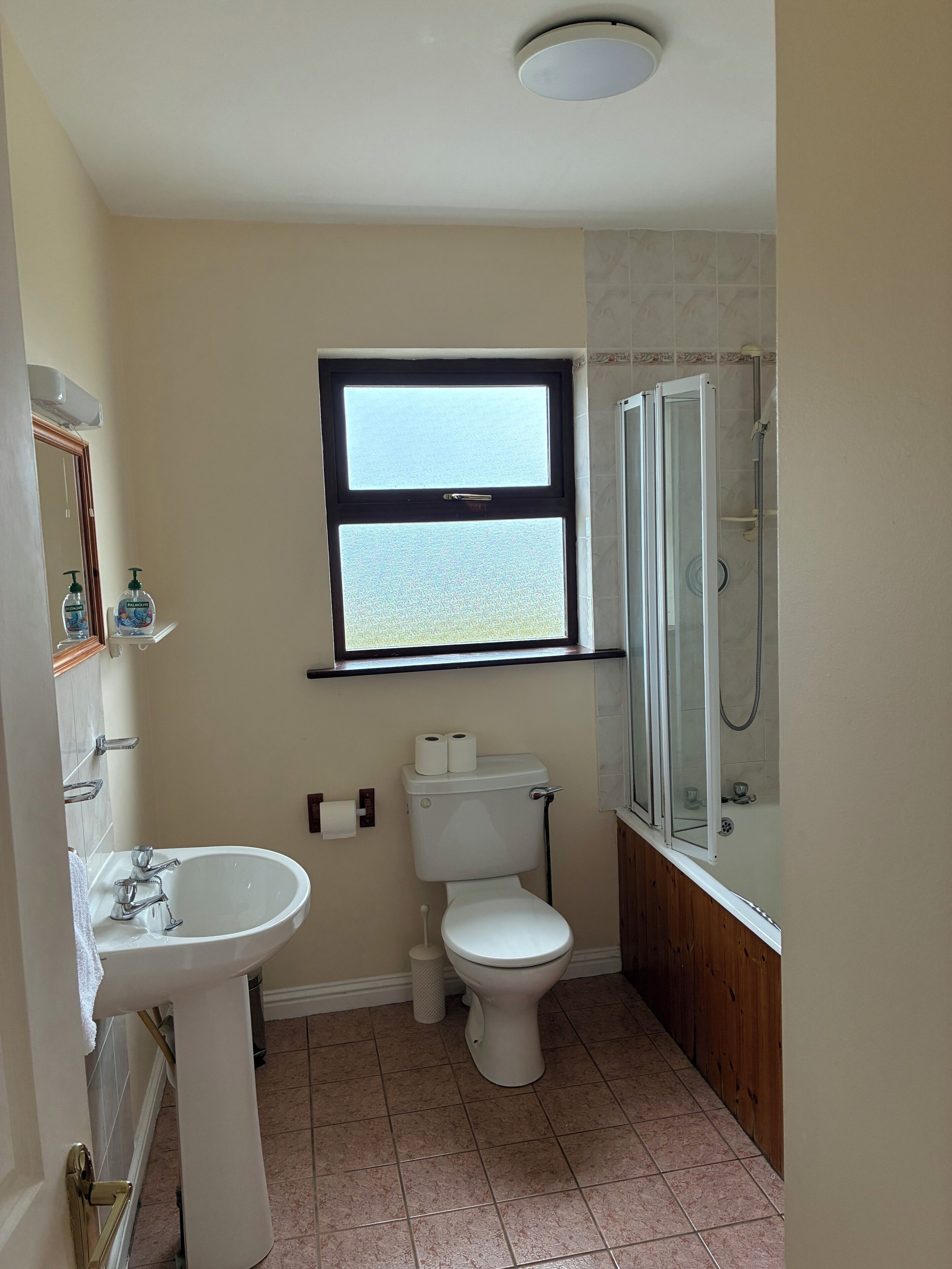 A bathroom with a sink, toilet, window, and shower.