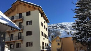 Un edificio a più piani con balconi, una facciata in pietra e un paesaggio montano innevato.