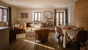 Un'ampia zona giorno con divano, poltrone, un tavolo da pranzo per quattro persone e un'ampia finestra con vista.