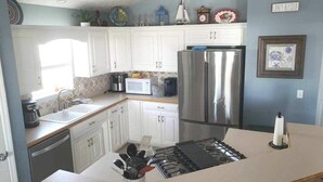 A compact kitchen with white cabinets, a stainless steel refrigerator, and a gas stove. - Beachside Blessings (1 Block From the Beach!) (Mexico Beach)