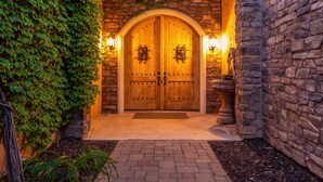A wooden double door with a stone archway, two wall-mounted lights, and a stone wall with ivy.
