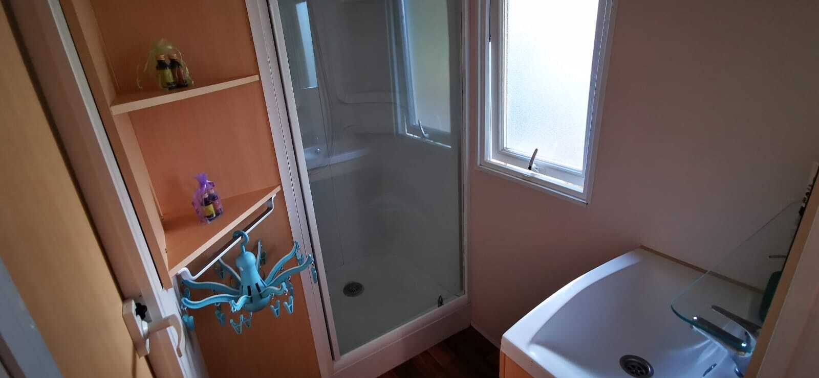 Une salle de bain avec une porte de douche en verre, une baignoire et une étagère contenant des articles de toilette.
