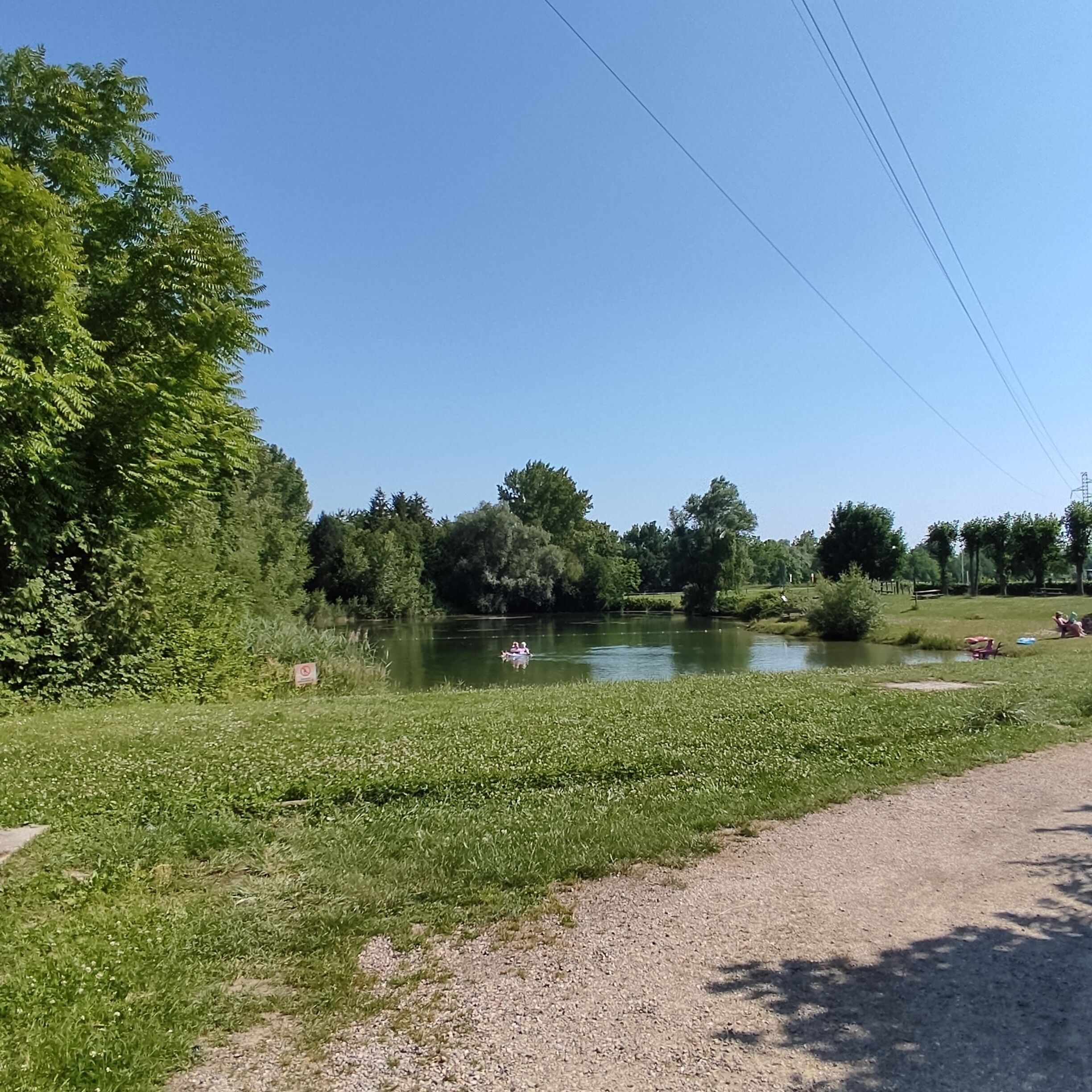 Un parc paisible au bord de la rivière, avec un sentier de gravier, une végétation luxuriante et une étendue d’eau calme.