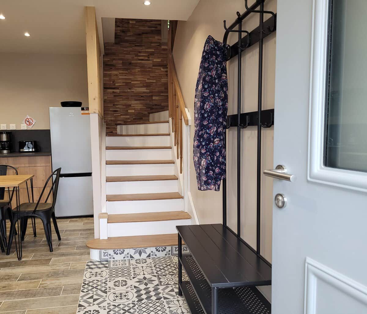 Eine Treppe führt zu einer zweiten Etage, einem Küchenbereich mit Kühlschrank und Herd sowie einem Teppich mit Muster auf dem Boden.