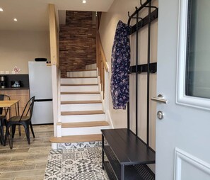 A staircase leading to a second floor, a kitchen area with a refrigerator and stove, and a patterned rug on the floor.