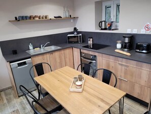 Cocina compacta con mesa de madera, microondas, cafetera y lavavajillas.