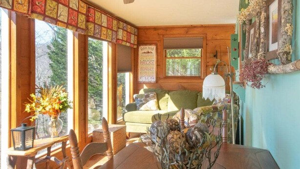 Interior acollidor d'una cabana amb taula de dinar de fusta, un sofà verd i una finestra gran amb vista a arbres.