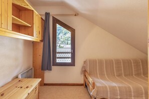 A small, cozy room with a sloped ceiling, a single bed, a wooden dresser, and a window with a view of a forested area. - 50m from ski slopes, 3rd floor, balcony, tv, ski locker, 38m², Valloire (Valloire)