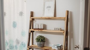 Una estantería de madera con toallas y una planta en maceta, frente a una pared blanca.
