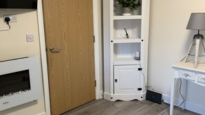 A room with a wooden door, a white cabinet with shelves, a mounted TV, and a desk with a lamp. - 2-bed Duplex Sleeps 3 With Fireplace (Doncaster)