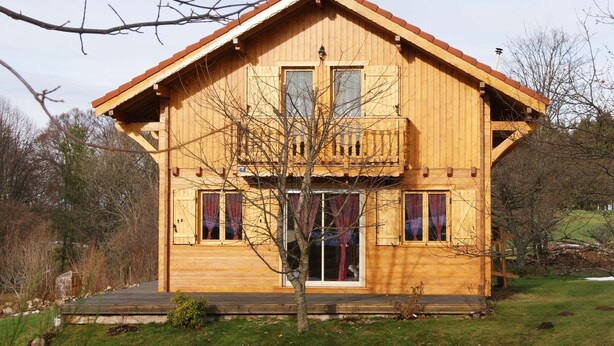 Eine Holzhütte mit Balkon, Veranda und großem Fenster.