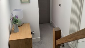 A hallway with a wooden bench, a vase with flowers, a framed picture on the wall, and a radiator. - Spacious and bright modern styling 3 bed flat (LONDON)