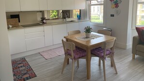 A modern kitchen with white cabinets, a wooden dining table, and a view of the outside. - Spacious and bright modern styling 3 bed flat (LONDON)