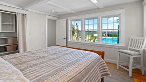 Ein Schlafzimmer mit einem großen Bett, einem Sessel, einem Schreibtisch und einem Fenster mit Blick auf einen Pool.